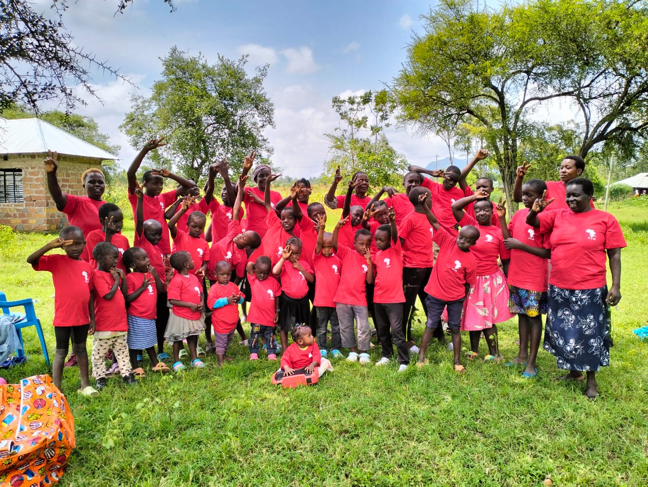 Energetic children and adults in red RDM.life t-shirts celebrating dance in Kenya, uplifting their community with joy and unity.