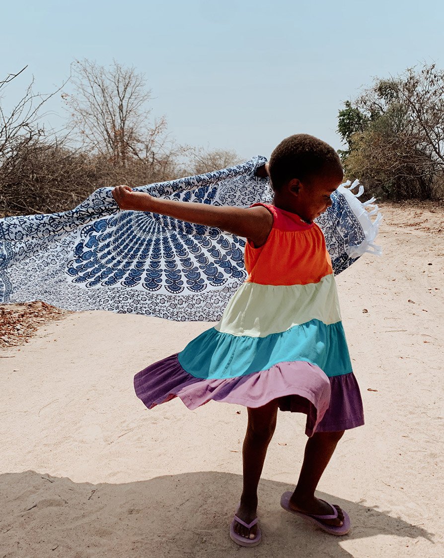 Young dancer from RDM's Muture, Zimbabwe chapter expressing joy through dance, with a patterned shawl against a natural backdrop.