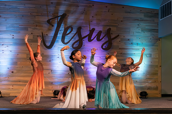 Dancers on stage at RDM's Castle Rock spring performance with 'Jesus' sign in the background, embodying worship through dance.