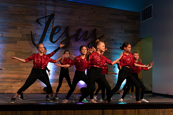 Energetic dance routine by RDM's performers with 'Jesus' sign backdrop, highlighting faith through dance at the Castle Rock spring event.