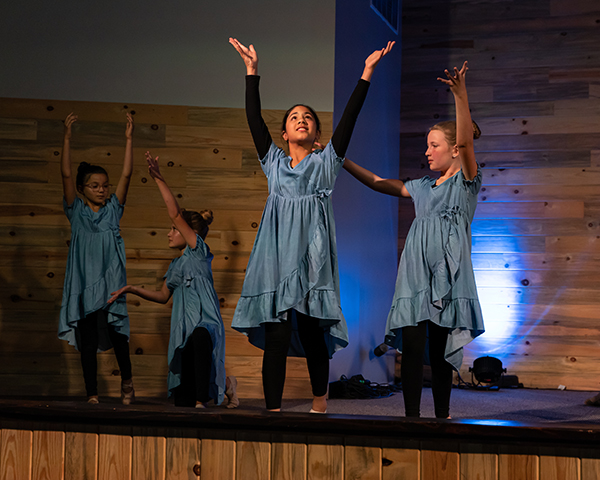 Dancers in blue dresses performing an uplifting routine at RDM's Castle Rock spring performance, celebrating worship through movement.