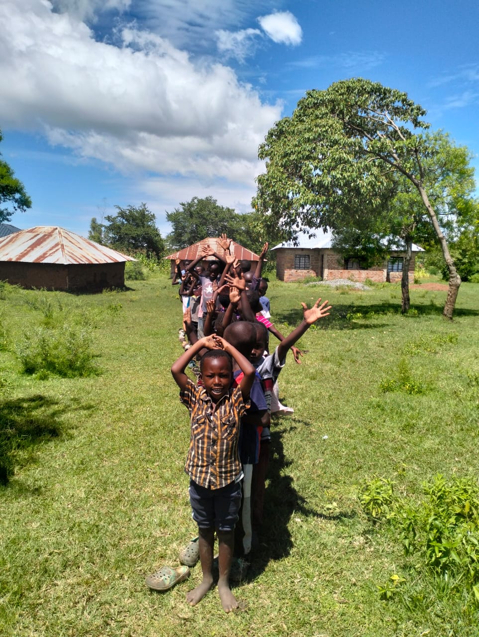 Joyful Kenyan children from RDM.life's EmpowerDance Collective raising their hands in the air, celebrating dance and life outdoors.