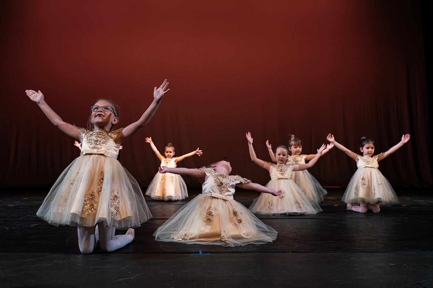 Young ballet dancers in golden costumes performing on stage with joyful expressions